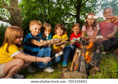 Happy friends near bonfire with marshmallow