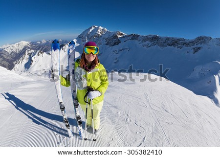 Happy woman in mask standing and holding ski and ski poles during sunny winter day on Krasnaya polyana ski resort and Caucasus mountains in Sochi, Russia