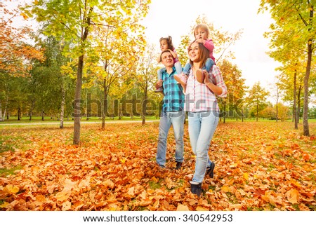 Mother and father carry little daughters in park