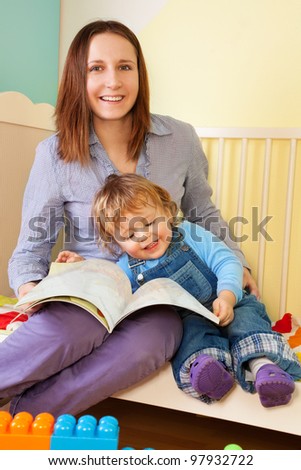 Mother reading a story from book to son toddler sitting in the bed