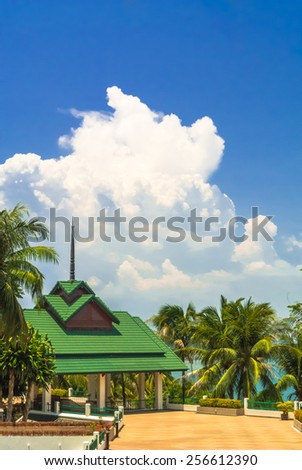Building and pathway between palm trees on cloudscape background.  \
Building and pathway.