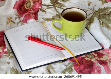 Green mug with tea or coffee in bed with bedding with floral print diary with a pencil or pen recording thoughts dreams