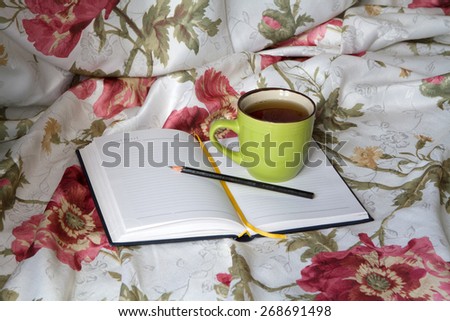Green mug with tea or coffee in bed with bedding with floral print diary with a pencil or pen note thoughts dreams