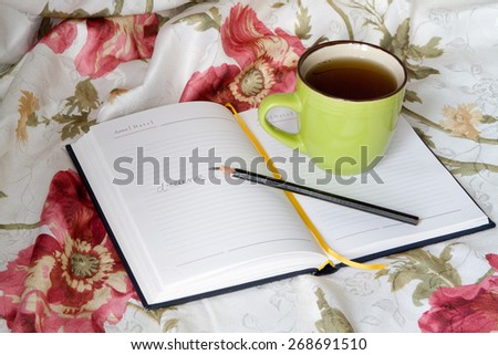 Green mug with tea or coffee in bed with bedding with floral print diary with a pencil or pen note thoughts dreams broken note
