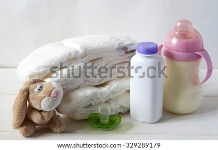 New born child stack of diapers, nipple soother, bunny toy and baby feeding bottle with milk on a white background
