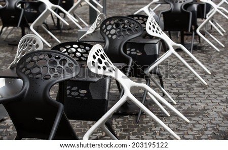 Black and white plastic chairs in a street cafe after rain in Italy