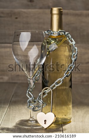Bottle of white wine and a glass shackled love chain with a lock.