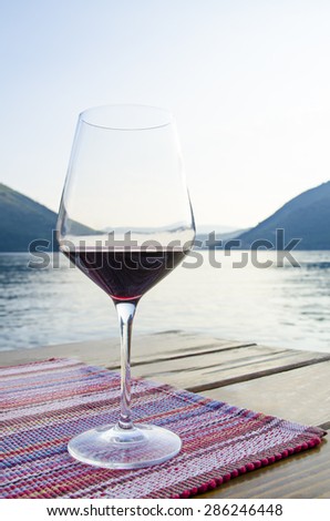 Close up view of the glass of red wine against blue sea and mountains during golden hour at sunset. Dinner on terrace in cafe.