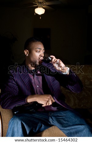 a hip young african american knocks back some wine on the couch while holding onto his bottle.