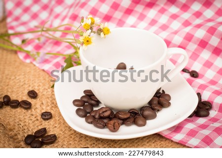 Cup of coffee beans and white flowers on the cloth sack and pink
