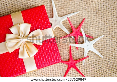 red gift box with gold  ribbon and star fish on sack background