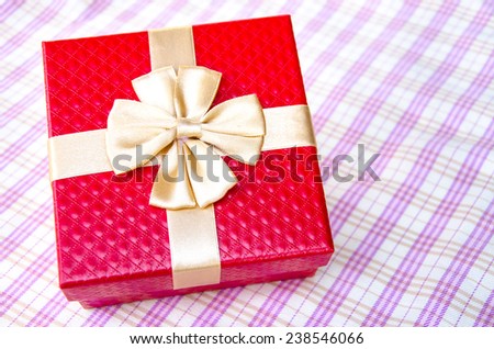 red gift box with gold ribbon on table background.