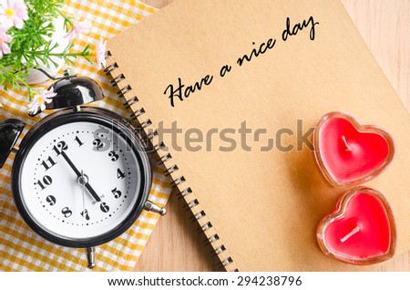 Have a nice day on brown diary and alarm clock with red heart on wooden background.