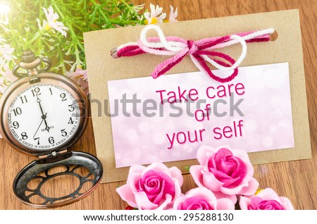 Take care of your self on tag and pocket watch with pink rose on wooden background.