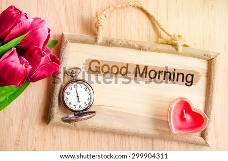 Good morning. Clock and red tulip with red candle heart shape on wooden background.