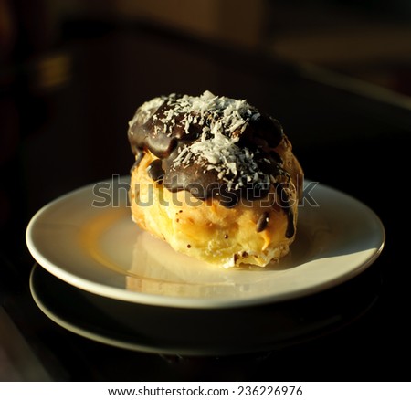 Eclairs with cream in chocolate coating on a plate on a dark background
