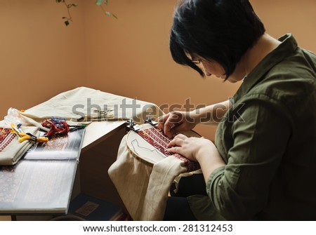 Hands women embroider on embroidery frame (cross stitch)