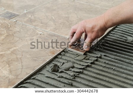 Man placing ceramic floor tile in position over adhesive