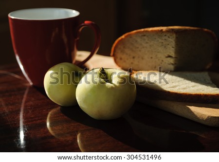 Still life. Two apples and bread on a board and red cup
