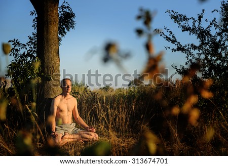 Man meditating. He sits under a tree legs folded under him