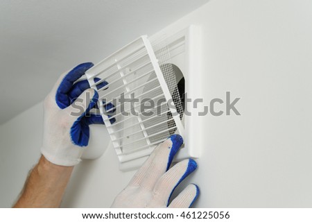 Worker installs ventilation grille on the wall.