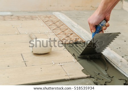 Worker installs  tiles on the floor. He put glue using comb trowel.
