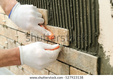 Installing the tiles on the wall. A worker putting tiles in the form of brick. He places the plastic crosses between the tiles.