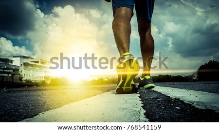 close up feet with running shoes and strong athletic legs of sport man, Athlete man in running pose on city street. Sport tight clothes. Bright sunset