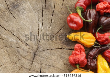 Various colorful hot peppers on a wooden background arranged on the side with space for content.