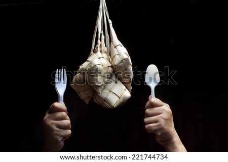 hand holding a fork and spoon to eat ketupat isolated  black background.Ketupat is traditional food in Malaysia for celebration