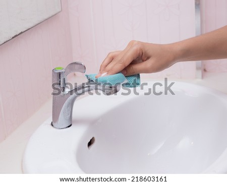 Hand with sponge cleaning white sink and faucet