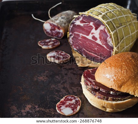 Cured pork shoulder  and salami over black metal surface.