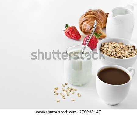 Breakfast with coffee, yogurt, oatmeal, croissant and strawberry.