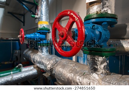 Red valve located on the flange of the blue pipe in the boiler room