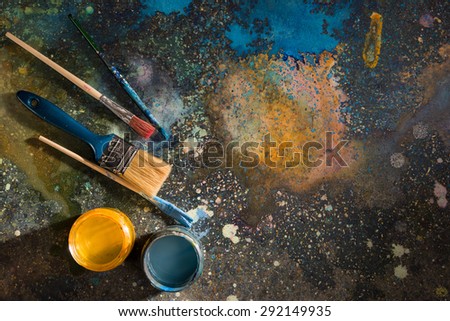 The palette of colorful paint splattered. On it are stained with paint brush and open cans of yellow and blue paint.