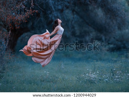 A young woman, a mysterious witch is floating in the air like a butterfly. A luxurious, long dress waving in the wind. Cold forest background. Enchanted princess. Art photo of levitation