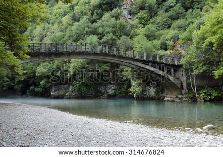 Old greece bridge over cristal clear blue water from the mountains not far from the village (Aristi) in the North of Greece.