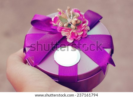 Purple round gift box tied by purple ribbon on hand with blank tag card.