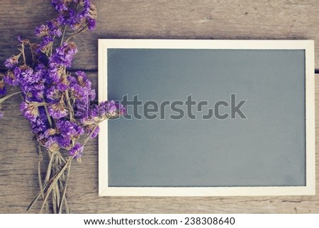 Blank blackboard on old wooden table with statice flowers, pastel filter