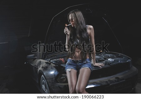 Super sexy chick smoking on the hood of old muscle american black car in garage