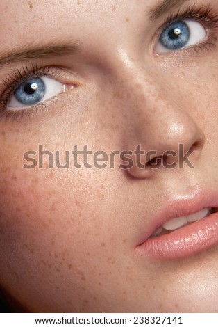 Close up beauty portrait of lassl with a lot of freckles, with fear in blue eyes, no makeup