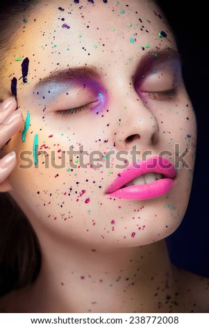 Facial portrait of young girl with a lot of blur of pain on her face, pink lipstick, purple eyeshadows closing her eyes and touching her temple on black background
