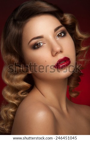 Beautiful portrait of young lady with brown eyes. Dark brown eye-shadows and deep red lipstick, two nevus on her right cheek and curly hair. Red background.