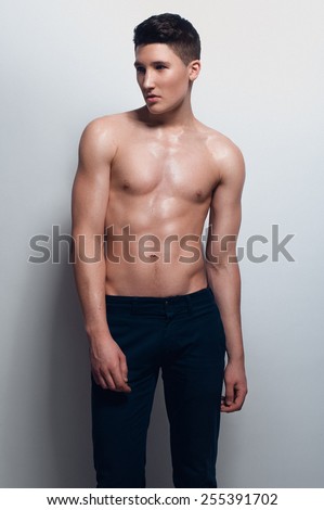 Fashion portrait of handsome dark haired boy with nude muscular body, no shirt, blue jeans, looking to the left on white background