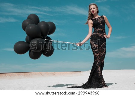 Fashion portrait of a young girl in a black dress with black balloons