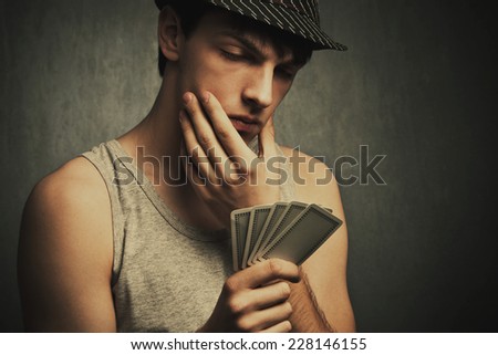 young man in tank top and hat watch his poker cards, studio shot