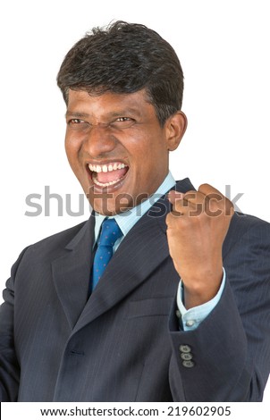A thrilled Indian / South Asian business executive in a suit cheering a win or victory with a big shout and clenched fist. Isolated on white background.