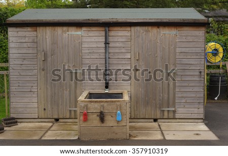 Wooden Garden Shed with a Hose Reel Attached at One End and Brushes for Cleaning Garden Tools in Devon, England, UK