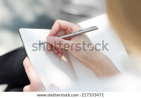Close-up of a female hand writing on an blank notebook with a pen.