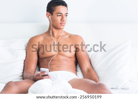 Young handsome topless black man enjoying music in bed.
